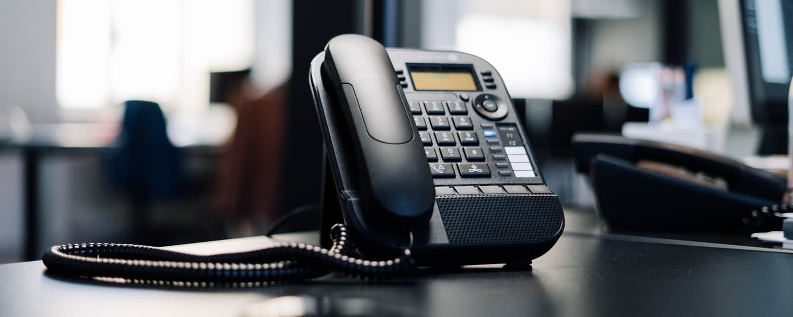 A desk phone with its handset in the cradle on an empty office desk.