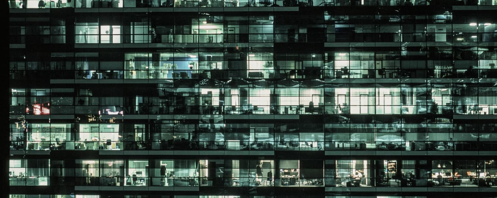 A glass office tower at night with most of its floors still lit.